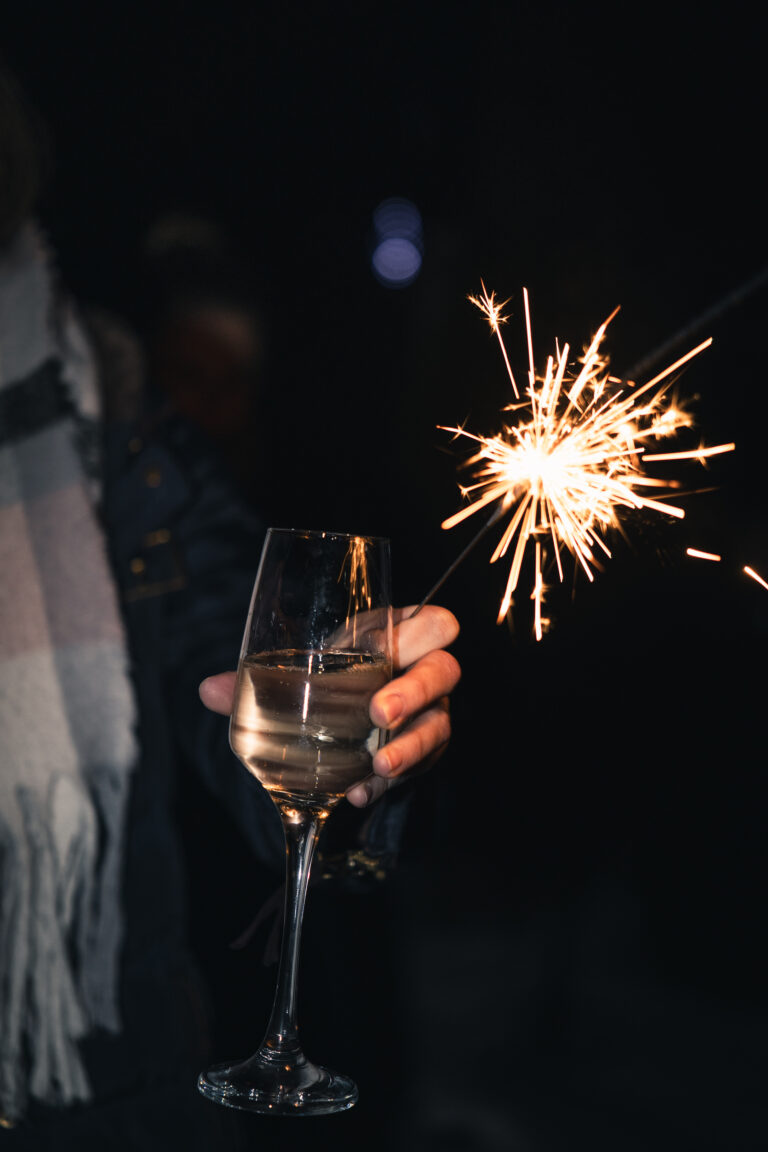 Strona główna Dłoń trzymająca kieliszek wina i palący się zimny ogień, nastrojowa fotografia.