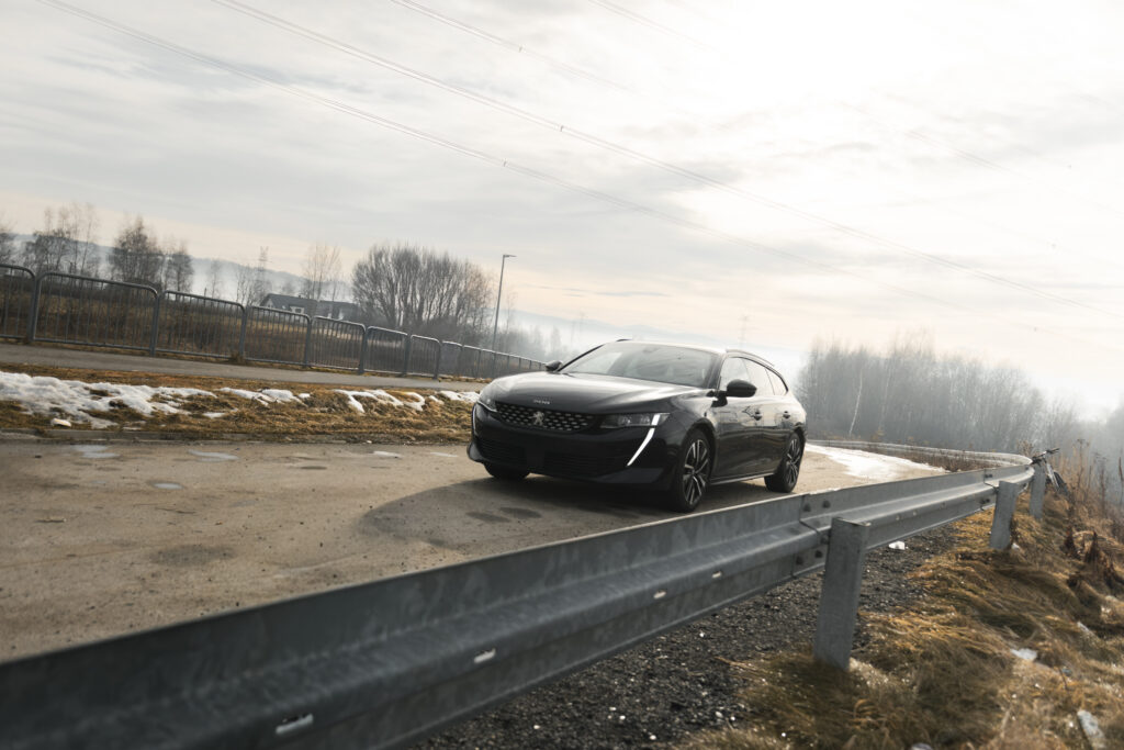 Samochód Peugeot jadący drogą obok barierki energochłonnej, profesjonalna fotografia.