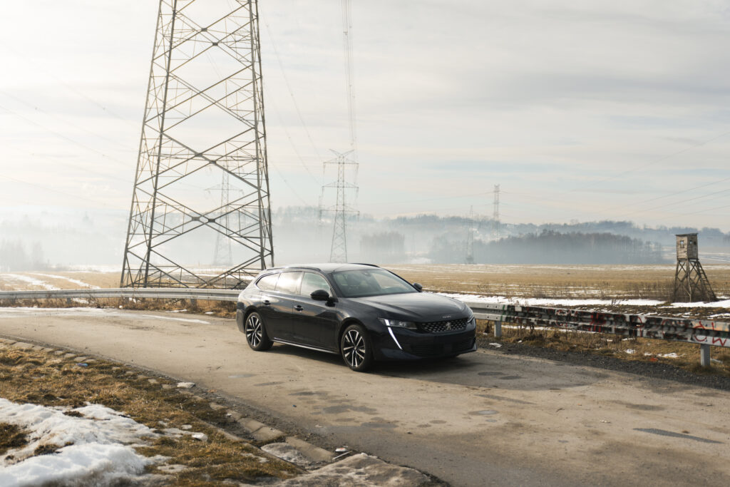 Sylwetka czarnego auta kombi na drodze przy wieży wysokiego napięcia, fotografia.