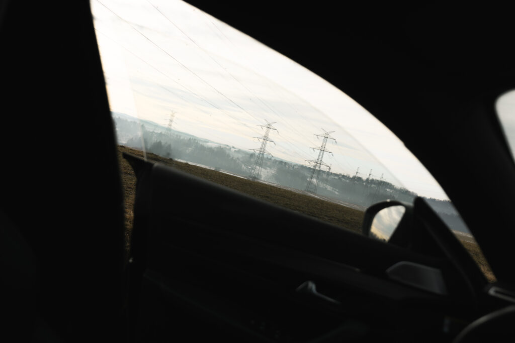 Widok przez szybę auta na zamglone pole i słupy wysokiego napięcia, fotografia.