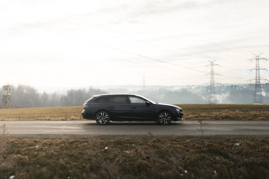Ciemny samochód kombi na pustej drodze, w tle pola i słupy energetyczne, fotografia.